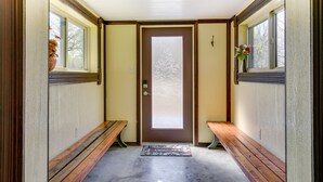 Un pasillo con un banco de madera a cada lado, una puerta con vidrio satinado y una ventana a la izquierda.