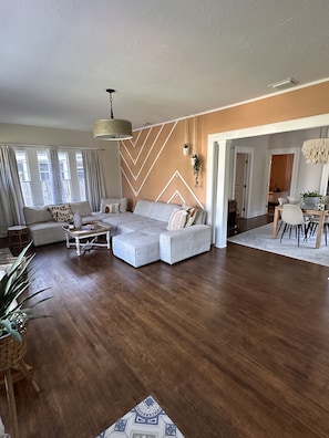 A spacious living room with a large sectional sofa, a coffee table, and a dining area with a wooden table and chairs.
