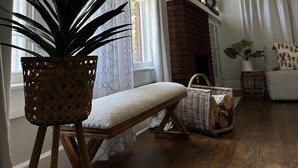 Ein gemütliches Wohnzimmer mit einer großen Topfpflanze, einer Bank, einem Kamin und einem Korbwannenmöbel.