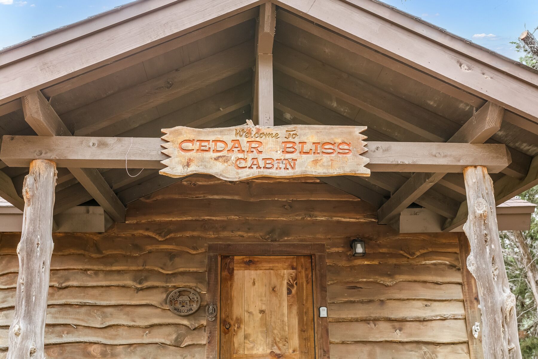 A wooden cabin with a sign reading "Welcome to Cedar Bliss Cabin."