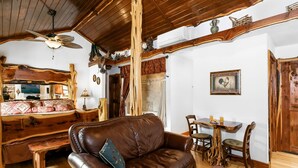 Una habitación rústica con techo de madera, un sofá de cuero marrón, una mesa de comedor de madera con sillas y un banco de madera.