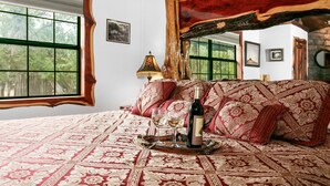 Un dormitorio con una cama grande, un cabecero de madera, una ventana y una mesita de noche con una botella y vasos.