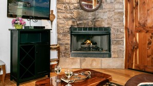 Una sala de estar con chimenea de piedra, un televisor montado en un mueble y una puerta de madera.