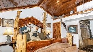 Una cama de madera rústica con un almohadón de estrella, un sofá de cuero y un techo de madera.