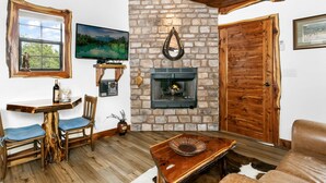 Una sala de estar acogedora con chimenea de piedra, muebles de madera y un televisor montado en la pared.