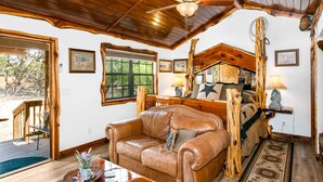 Una habitación acogedora con techo de madera, un sofá de cuero, estructura de cama de madera y una mesa de comedor con un jarrón de flores.