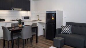 Una cucina moderna con mobili scuri, un forno a microonde, un lavello e un frigorifero. C'è un tavolo da pranzo con sedie e un divano grigio con un cuscino decorato.