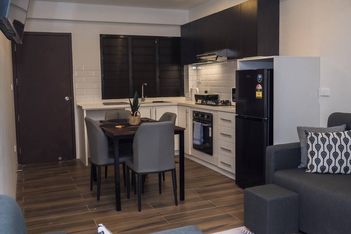 A compact kitchen with dark cabinets, a refrigerator, and a dining area with chairs and a table.