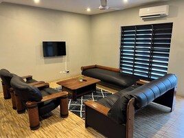 Un salon moderne comprenant un canapé, deux fauteuils, une table basse et un téléviseur fixé au mur.