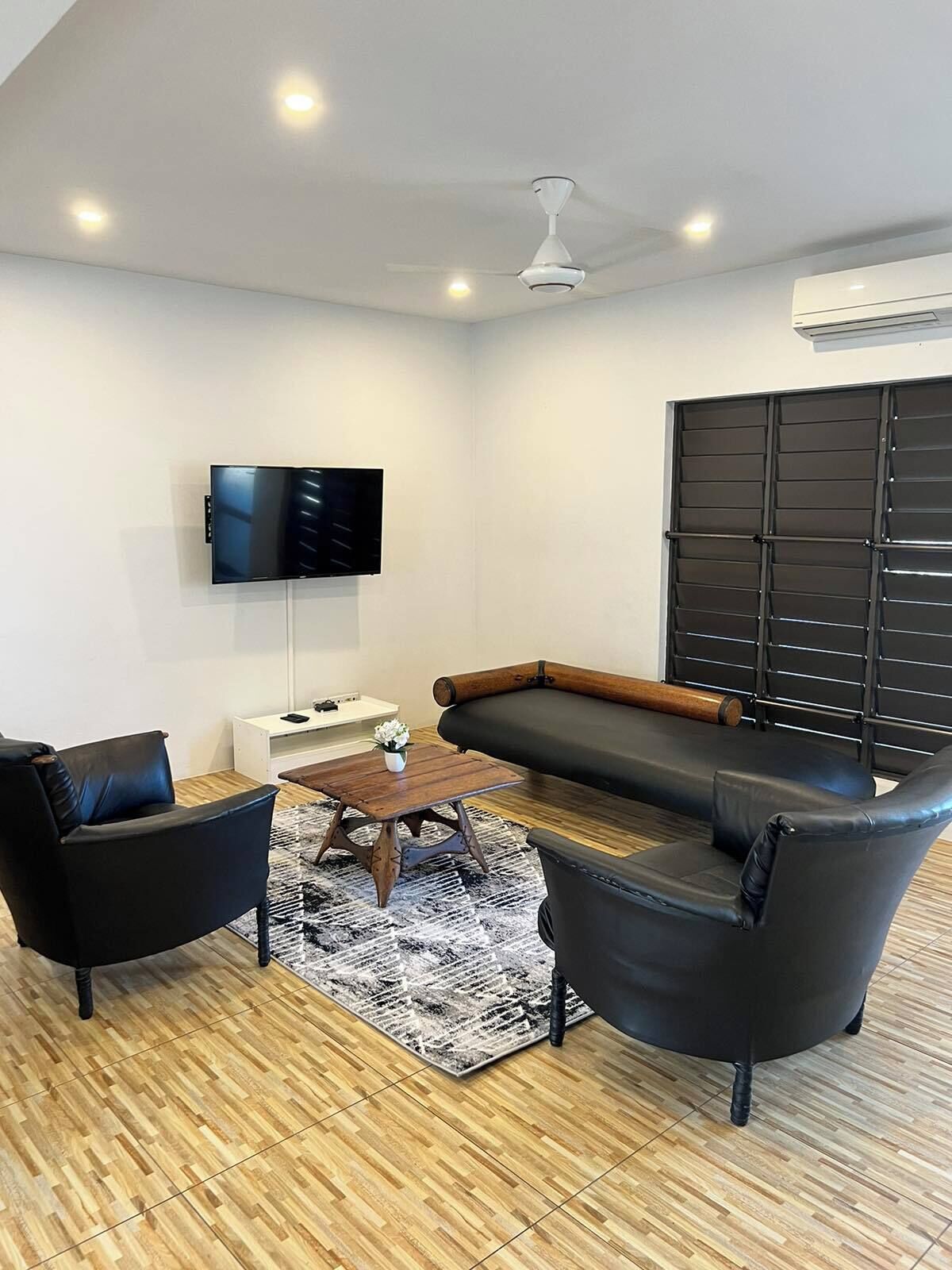 Un salon moderne doté d’un téléviseur à écran plat, d’un canapé, de deux fauteuils, d’une table basse et d’un tapis à motifs.