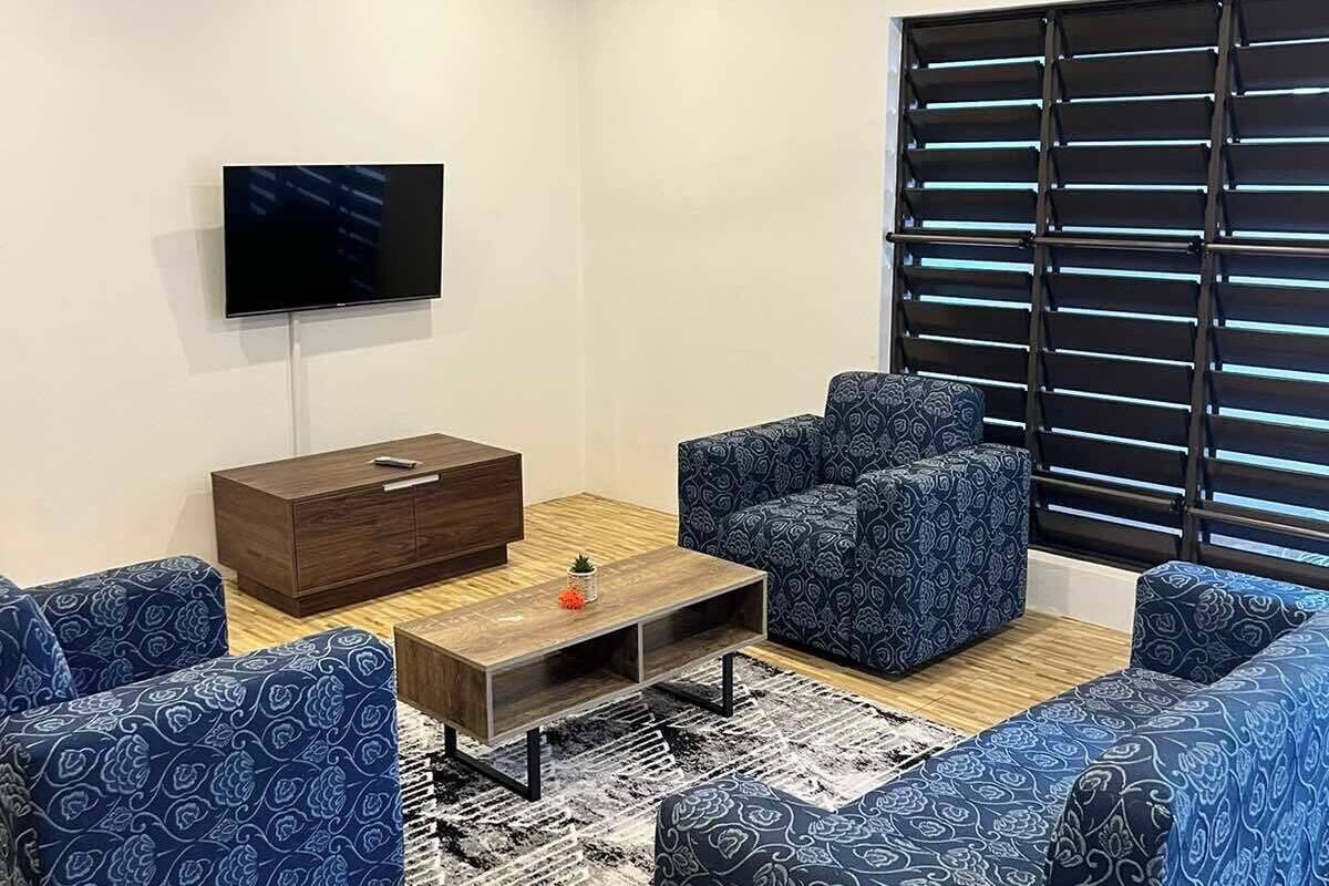 A modern living room with a flat-screen TV, a ceiling fan, and a large window with blinds.
