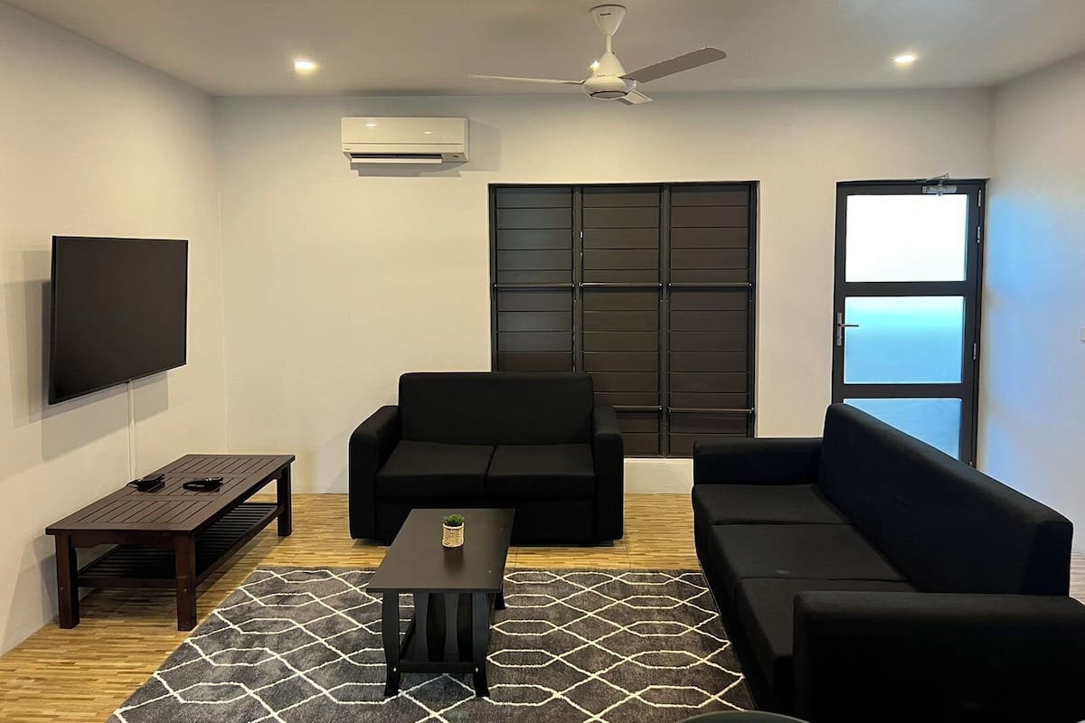A modern living room with a flat-screen TV, a ceiling fan, a black sofa, a coffee table, and a patterned rug.