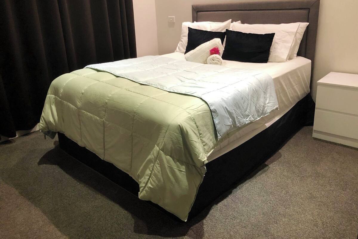 A neatly made bed with a green and white duvet, black and white pillows, and a grey headboard.