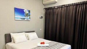 Un letto rifatto con lenzuola bianche e una coperta a righe, un quadro raffigurante una spiaggia sulla parete e una tenda scura che copre una finestra.
