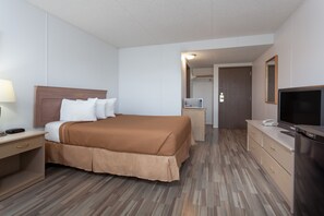 Une chambre d’hôtel comprenant un lit, une table de chevet, une télévision et un petit bureau avec une lampe.