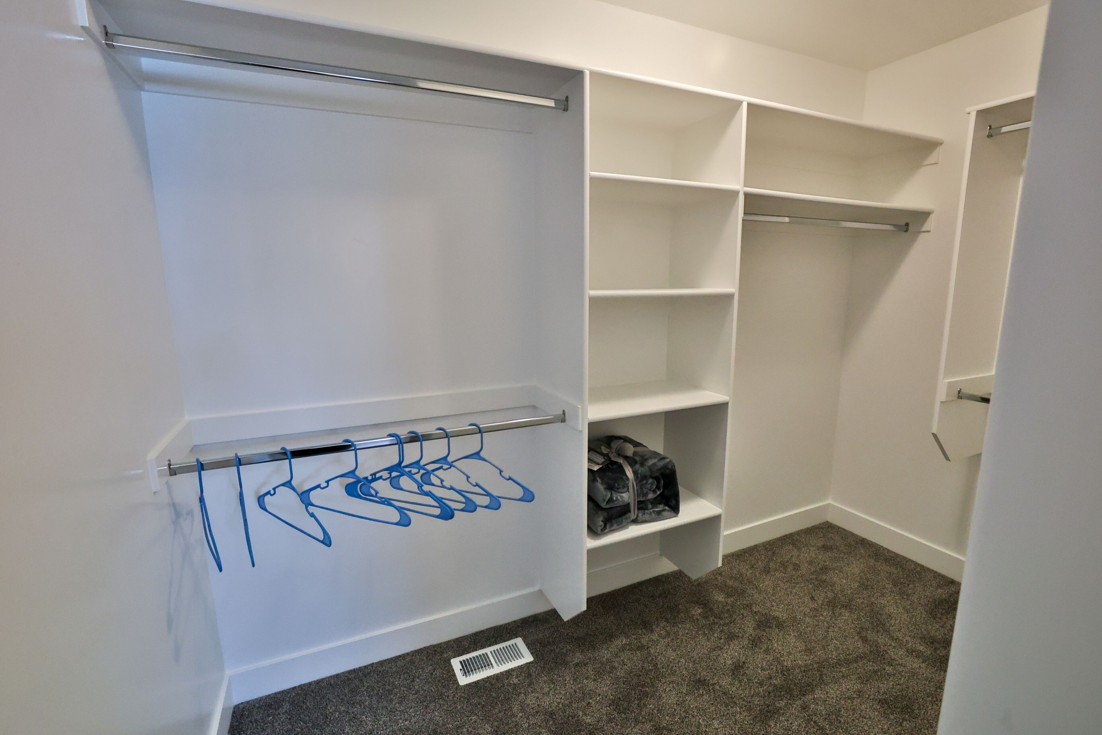A walk-in closet with open shelves, a hanging rod, and a vent on the floor.