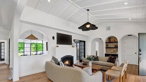 Ein geräumiges Wohnzimmer mit Kamin, einer großen Couch, einem Couchtisch und einem an der Wand befestigten Fernseher.