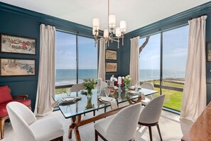 A dining area with a glass table, white chairs, and a view of the ocean. - Luxury Beachfront Condo with Remarkable Ocean Views! (Santa Barbara)