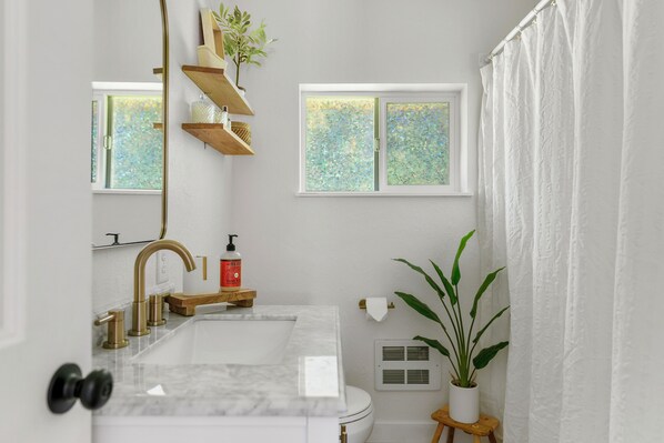 A bathroom with a marble sink, gold faucet, wooden shelves, a potted plant, and a window with frosted glass. - Riverfront Retreat in Thompson Falls (Thompson Falls)