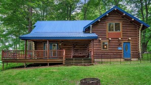 A rustic log cabin with a porch and a fire pit in front.