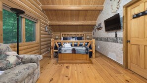 A log cabin bedroom with a bed, a couch, a ceiling fan, and a TV mounted on the wall.