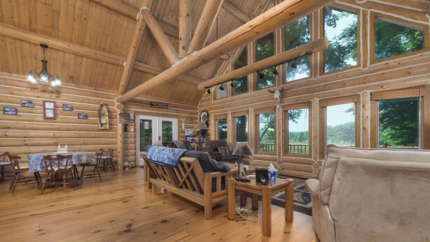 A log cabin interior with a dining area, sofa, and large windows.