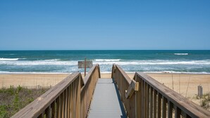 Une promenade en bois qui mène à une plage où l’on peut voir des vagues.