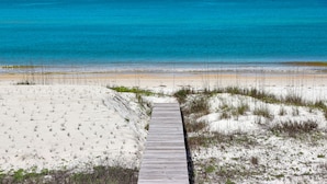 Un paseo marítimo de madera que conduce a una playa arenosa con agua azul cristalina.