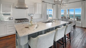 Una cocina moderna con una isla grande, armarios blancos y vistas al océano.