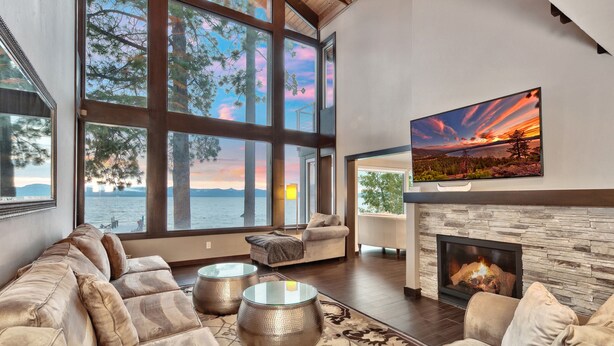 A spacious living room with a large window overlooking a lake, a fireplace, and a comfortable seating area.