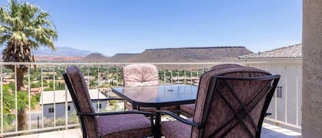 A balcony with a table and chairs, overlooking a landscape with mountains and a palm tree.