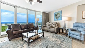 A spacious living room with a large window offering a view of the ocean, a ceiling fan, and a mix of leather sofas and armchairs. - Caribe Resort C712 | Lazy River, Pools, Hot Tubs, Gym, Tennis | Waterfront Condo | Beach Getaways (Orange Beach)