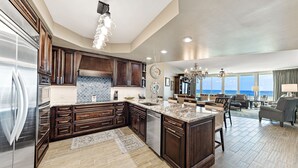 A spacious kitchen with dark wood cabinets, a large island, and a view to the living area. - Caribe Resort C712 | Lazy River, Pools, Hot Tubs, Gym, Tennis | Waterfront Condo | Beach Getaways (Orange Beach)