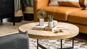 A round wooden coffee table with a book, a small potted plant, and a string of beads.