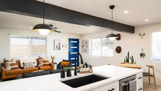 A modern kitchen with a white countertop, black faucet, and pendant lighting. There is a blue door and a wall-mounted cactus decoration.