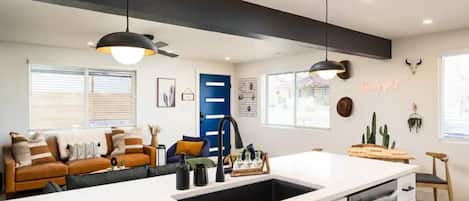 A modern kitchen with a white countertop, black faucet, and pendant lighting. There is a blue door and a wall-mounted cactus decoration.