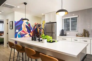 Una cucina moderna con isola centrale, sgabelli da bar, frigorifero e un'ampia finestra con persiane.
