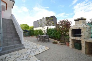 A patio with a stone fireplace, outdoor seating, and a staircase leading to a building.