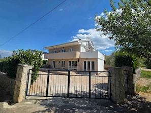 Una casa de dos pisos con techo plano, balcón y entrada protegida por una reja.