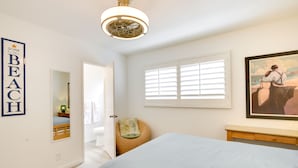 A bedroom with a bed, a bedside table, a chair, a window with blinds, a painting, and a wall-mounted mirror. - San Diego Home w/ Deck: Walk to Mission Beach! (San Diego)