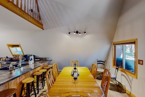 A dining area with a wooden table, bar stools, and a lantern. There is a staircase with wooden railings and a ceiling light fixture.