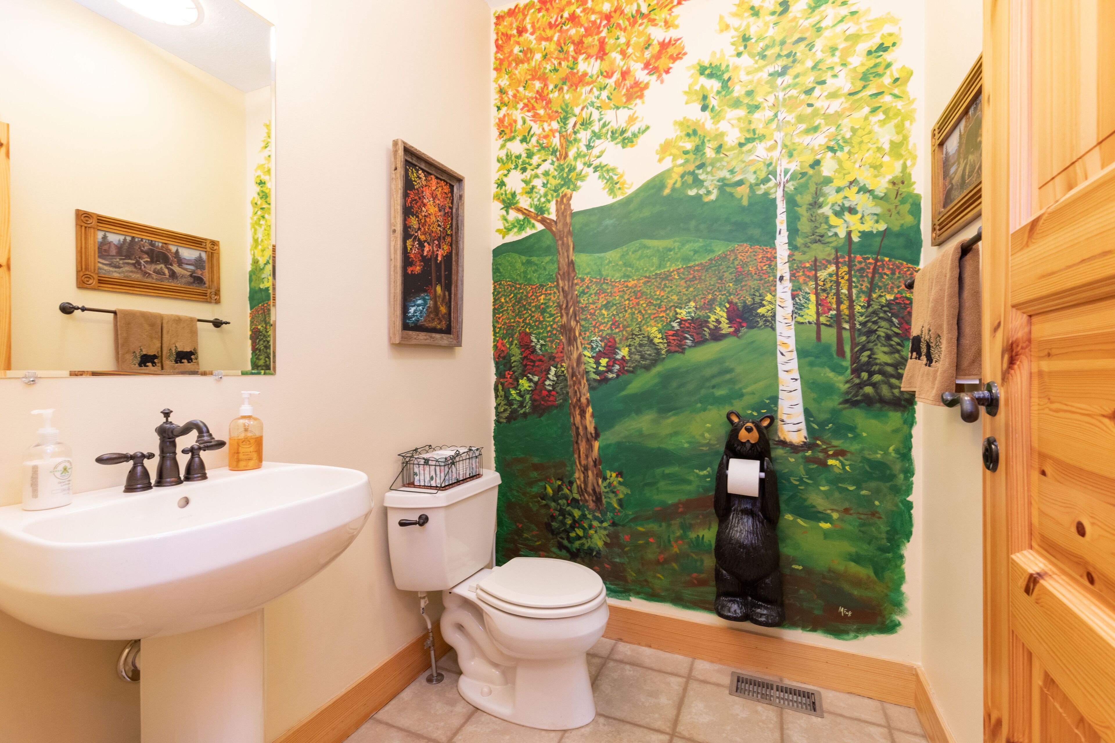 Een badkamer met een wastafel, toilet en een muurschildering van een boslandschap.