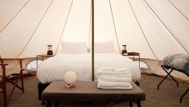 A tent-style room with a bed, bedside tables, a bench, and a round light fixture. - Deluxe Leaf Bell Tent (Clydesdale)