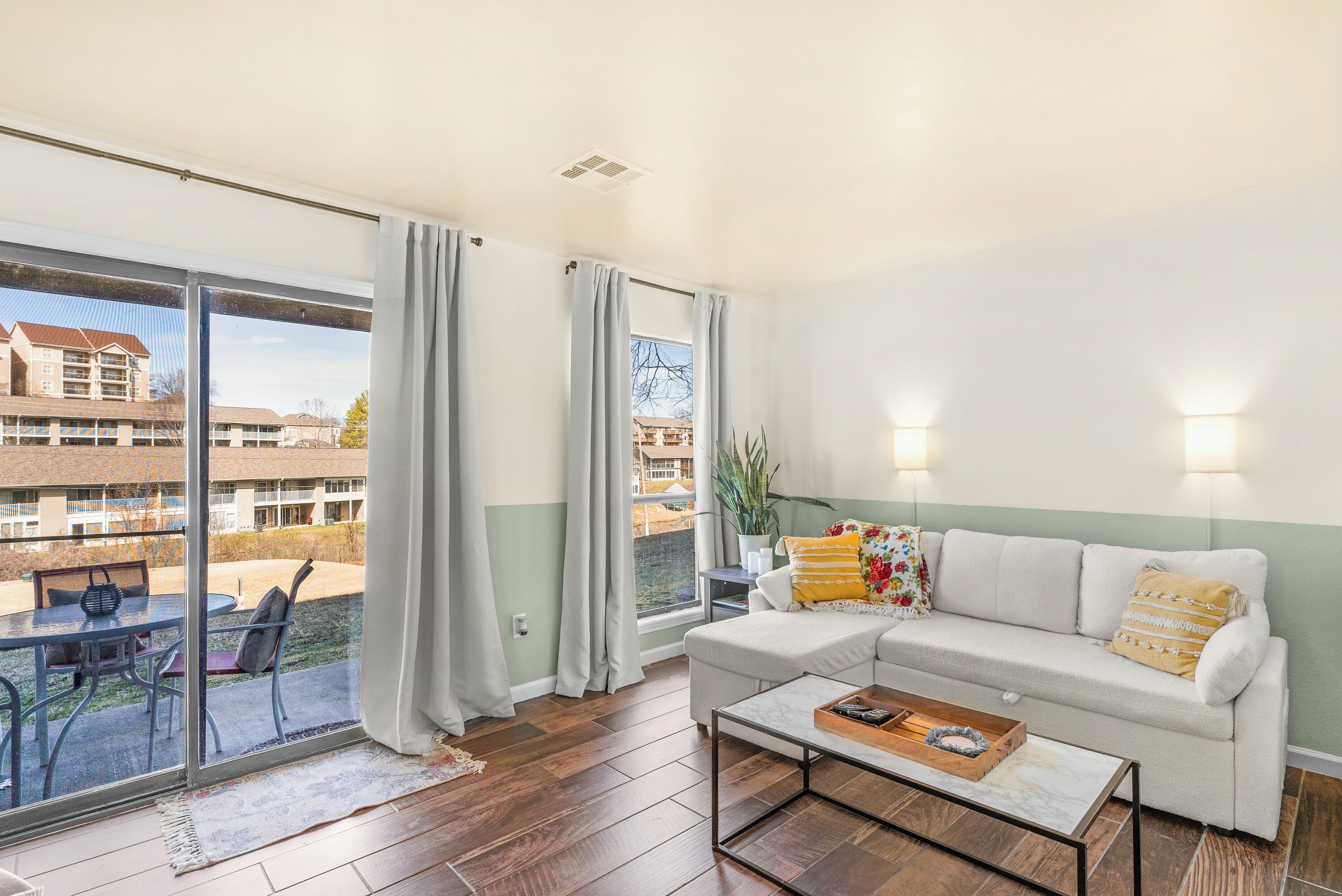 A living room with a sofa, coffee table, and a view of a courtyard through large windows.