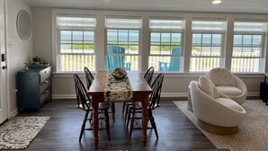 Un comedor con una mesa de madera, sillas y vistas a la playa a través de amplios ventanales.