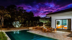 Zona de piscina exterior moderna amb una piscina nítida, gandules de fusta i un porxo ben il·luminat.