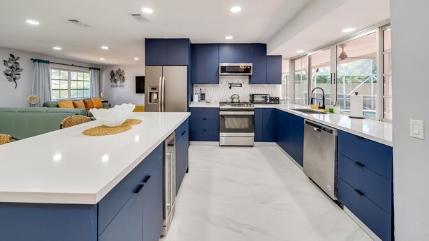 A modern kitchen with blue cabinets, a white countertop, stainless steel appliances, and a large window providing natural light. - MODERN HOME WITH HEATED POOL! CLOSE TO SAWGRASS MILLS MALL! FLEXIBLE CHECK IN 
  (Sunrise)