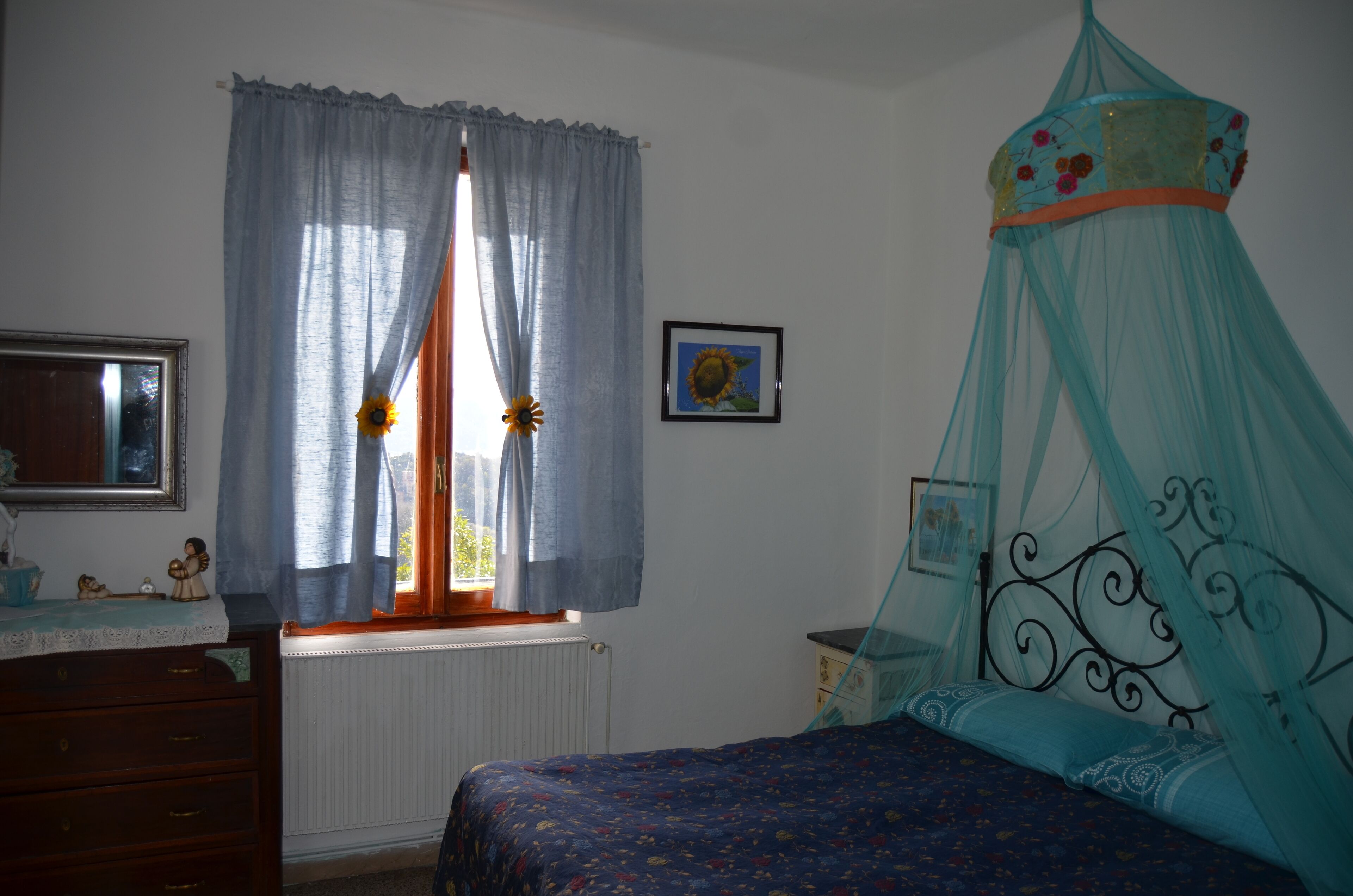 Une chambre à coucher avec un lit, une commode, une fenêtre avec des rideaux et un tableau accroché au mur.