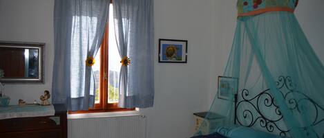 Une chambre à coucher avec un lit, une commode, une fenêtre avec des rideaux et un tableau accroché au mur.