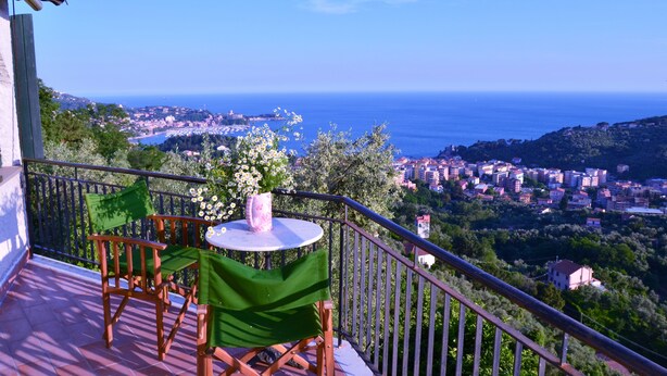 Un balcon avec une table et des chaises, donnant sur une ville côtière et la mer.